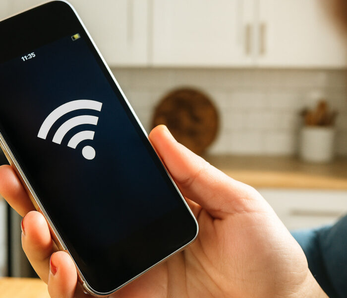 Oseba drži pametni telefon z velikim Wi-Fi simbolom na zaslonu v kuhinji, kar ponazarja težavo »android wifi ne deluje«.